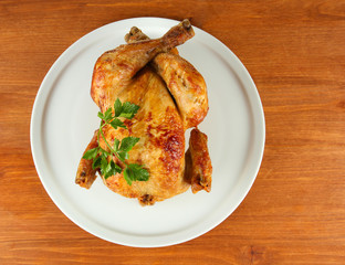 Roasted whole chicken on a white plate on wooden background