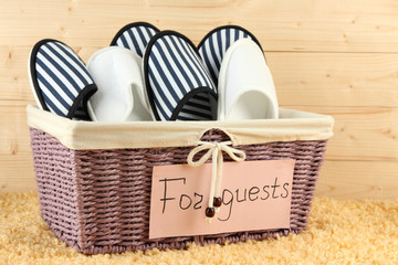 Slippers in basket on carpet on wooden background