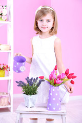 Beautiful little girl and stand with flowers on pink background