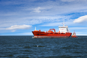 A huge red oil tanker and a tugboat at work.