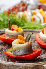 Pickled herring rolls with vegetables on wooden tray