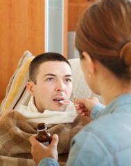 woman giving cough syrup to unwell man