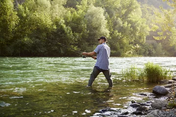 Poster Fischer, der in der Nähe eines Flusses steht und eine Angelrute hält © Diego Cervo