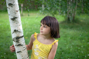 The girl is standing under a tree and looks in the direction of