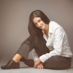 Young elegant woman sitting against grey background