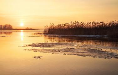 Winter landscape with river and sunset fiery sky.