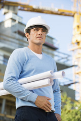 Male architect with rolled up blueprints standing at construction site