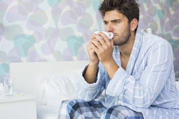 Sick man drinking coffee while sitting on bed at home