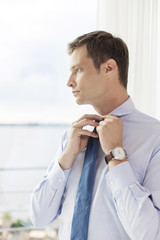 Thoughtful businessman adjusting necktie in hotel