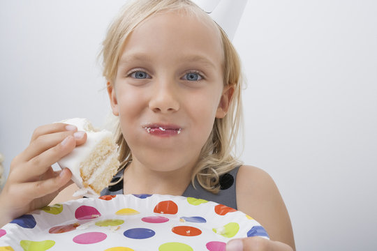 Close-up of cute girl eating birthday cake against gray background