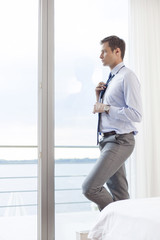Thoughtful businessman adjusting necktie in hotel