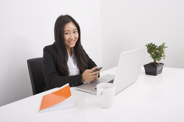 Portrait of smiling businesswoman using cell phone at office desk