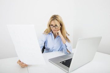 Businesswoman in eyeglasses reading document at office desk
