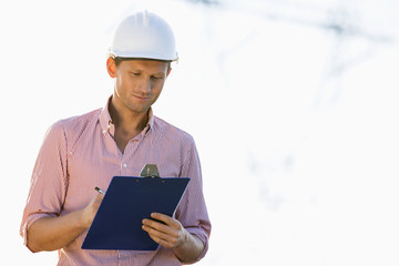 Male architect writing on clipboard at site