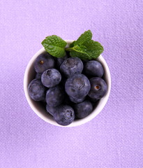 Blueberries with mint in white bowl on purple background