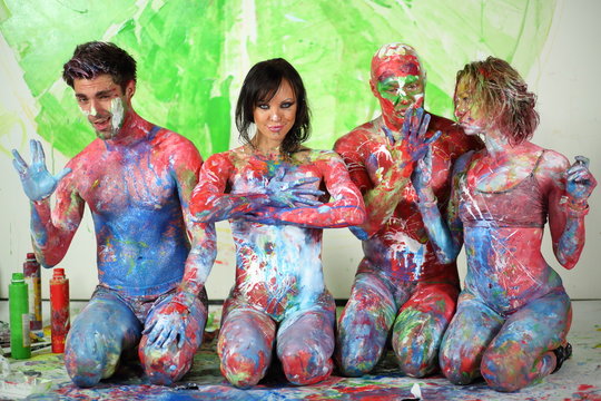 Four people sitting on floor in studio with whole body in paint