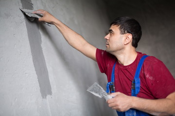 worker with spatula makes repairs smears on wall putty