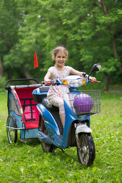 Little girl on a unreal design scooter with empty cart