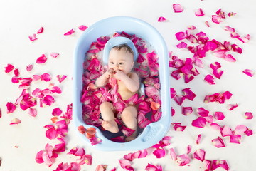 Fototapeta premium Baby girl lies in a bathtube with rose petals in studio