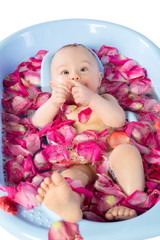 Beautiful baby girl lies in a bathtube with rose petals