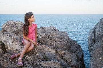 The little girl is sitting on the rocks near the sea