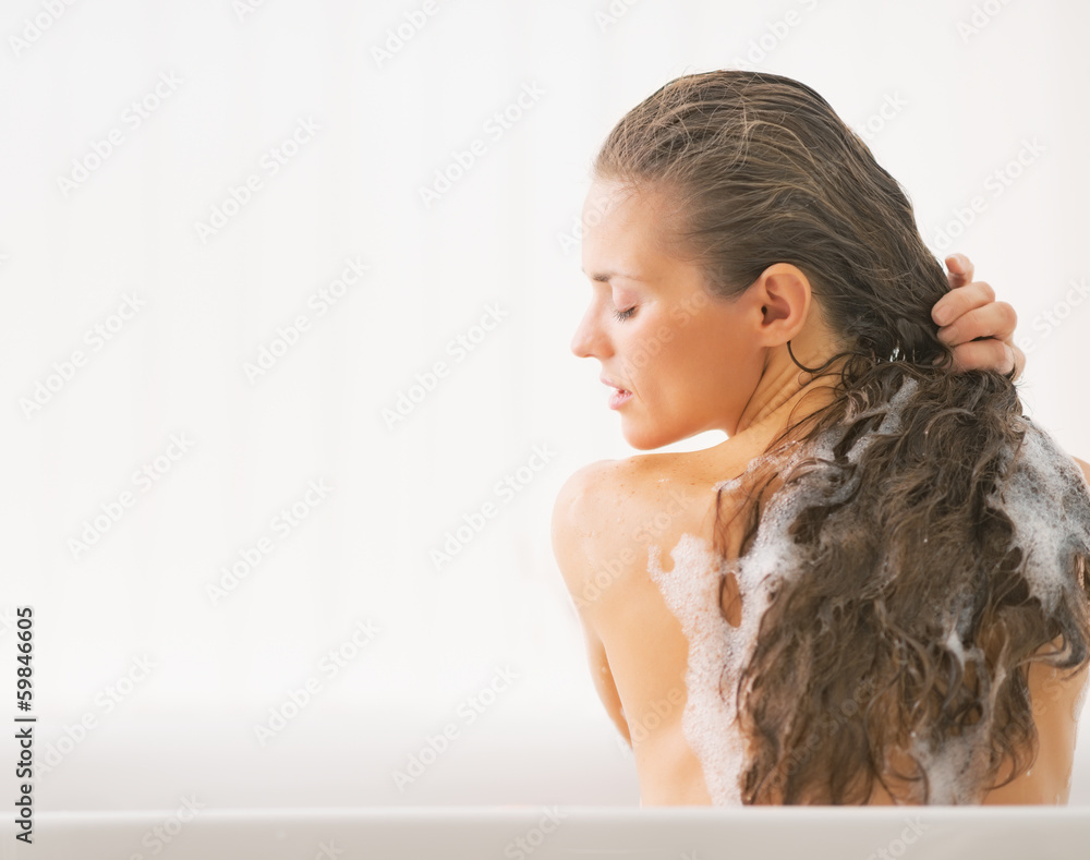 Wall mural young woman washing hair in bathtub