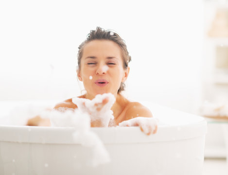 Happy young woman playing with foam in bathtub