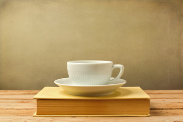 Coffee cup on book on wooden table over grunge background