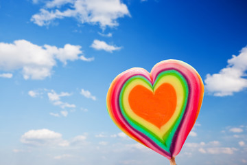 Colorful heart shaped lollipop on sky background