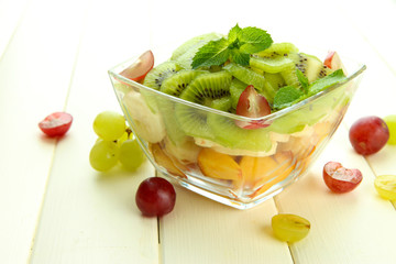 Tasty fruit salad in glass bowl, on white wooden table