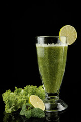 Glass of green vegetable juice and lime isolated on black