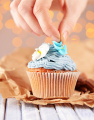 Confectioner decorating tasty cupcake with butter cream,