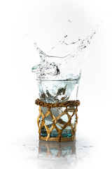 Glaçon qui tombe dans un verre, l'eau déborde et proque des é