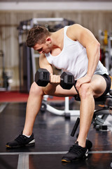 Fototapeta na wymiar Handsome man working with heavy dumbbells in the gym