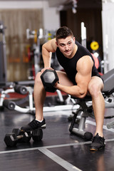 Fototapeta na wymiar Athletic man working with heavy dumbbells at the gym