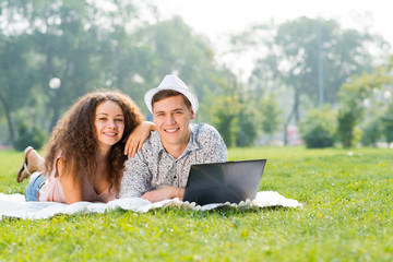 couple lying together in a park with laptop