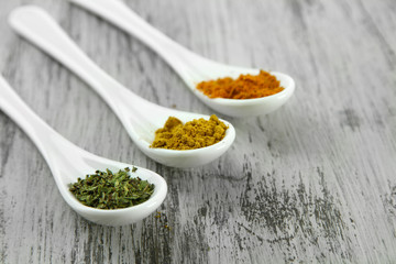Assortment of spices in  white spoons, on wooden background