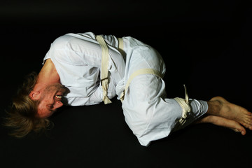 Mentally ill man in strait-jacket on black background