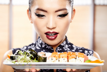 Plakaty  Piękna młoda kobieta jedzenie sushi. Mała głębia ostrości, ostrość