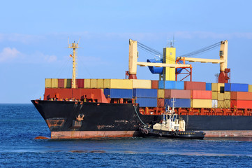 Tugboat assisting container cargo ship to harbor quayside
