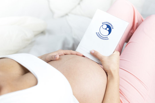 Schwangere Frau liegend h&auml;lt  Babybauch und Mutterpass