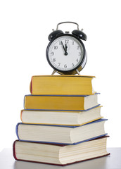 Naklejka premium A stack of books with an alarm clock on top.