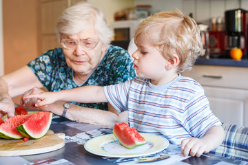 Little toddler boy and his great grandmother eating watermelon a