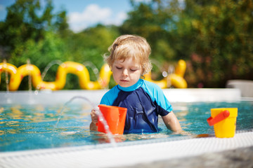 Cute toddler playing with water by the outdoor swimming pool