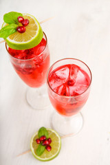 Two glasses with red pomgranate champagne, lime and mint.