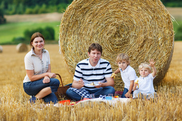 happy family of four picnicking on yellow hay field in summer.