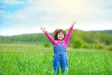 Naklejka na ściany i meble Happy little girl with her hands up on the green wheat field
