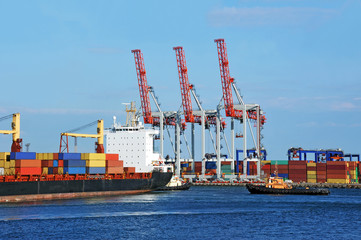 Tugboat assisting container cargo ship to harbor quayside