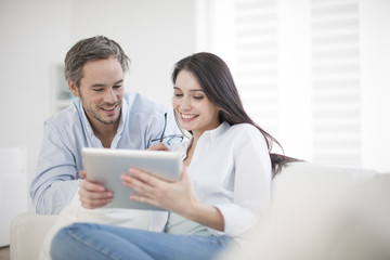 Cheerful couple using digital tablet at home - obrazy, fototapety, plakaty