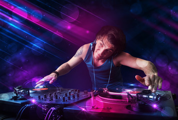 Young DJ playing on turntables with color light effects